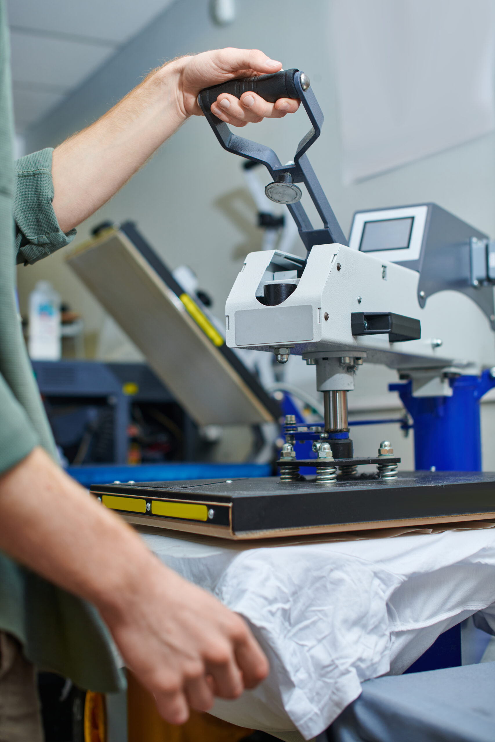 A worker operating a professional heat press machine to apply custom designs onto a white t-shirt, illustrating heat press shirt printing in Houston, TX.