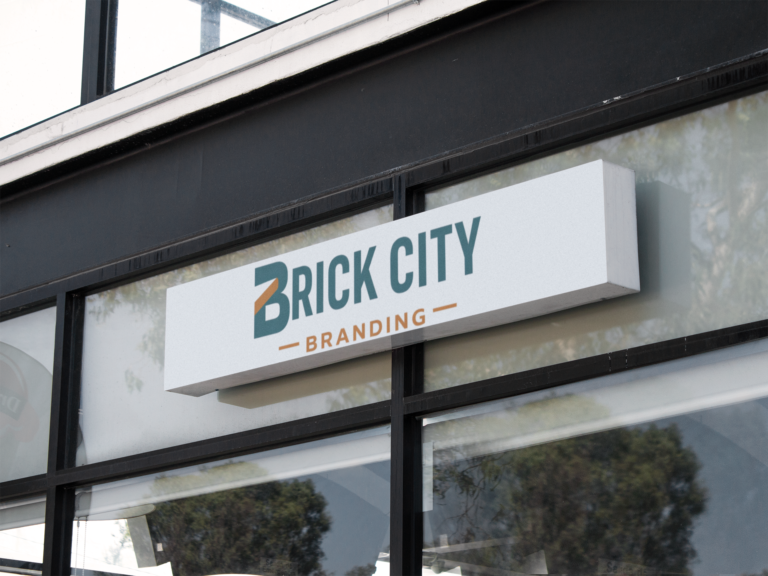 A horizontal white rectangular outdoor sign for "Brick City Branding" mounted on a modern black storefront, featuring a teal and orange "B" logo.