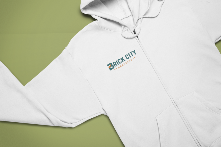 A white zip-up hoodie featuring a printed logo for Brick City Branding laid on a olive green background, demonstrating custom hoodie printing in Philadelphia, PA.