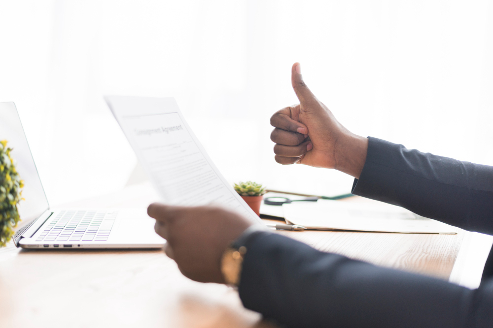 A professional holding a document titled Employment Agreement and giving a thumbs up at a desk with a laptop, representing contract attorney services in Atlanta, GA.