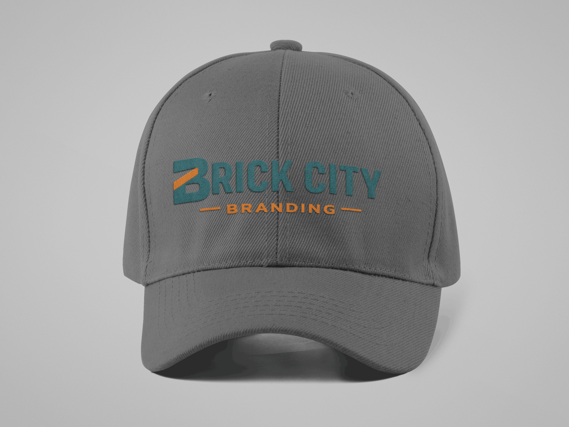 A charcoal grey 6-panel baseball cap with the "Brick City Branding" logo embroidered directly onto the front in teal and orange.