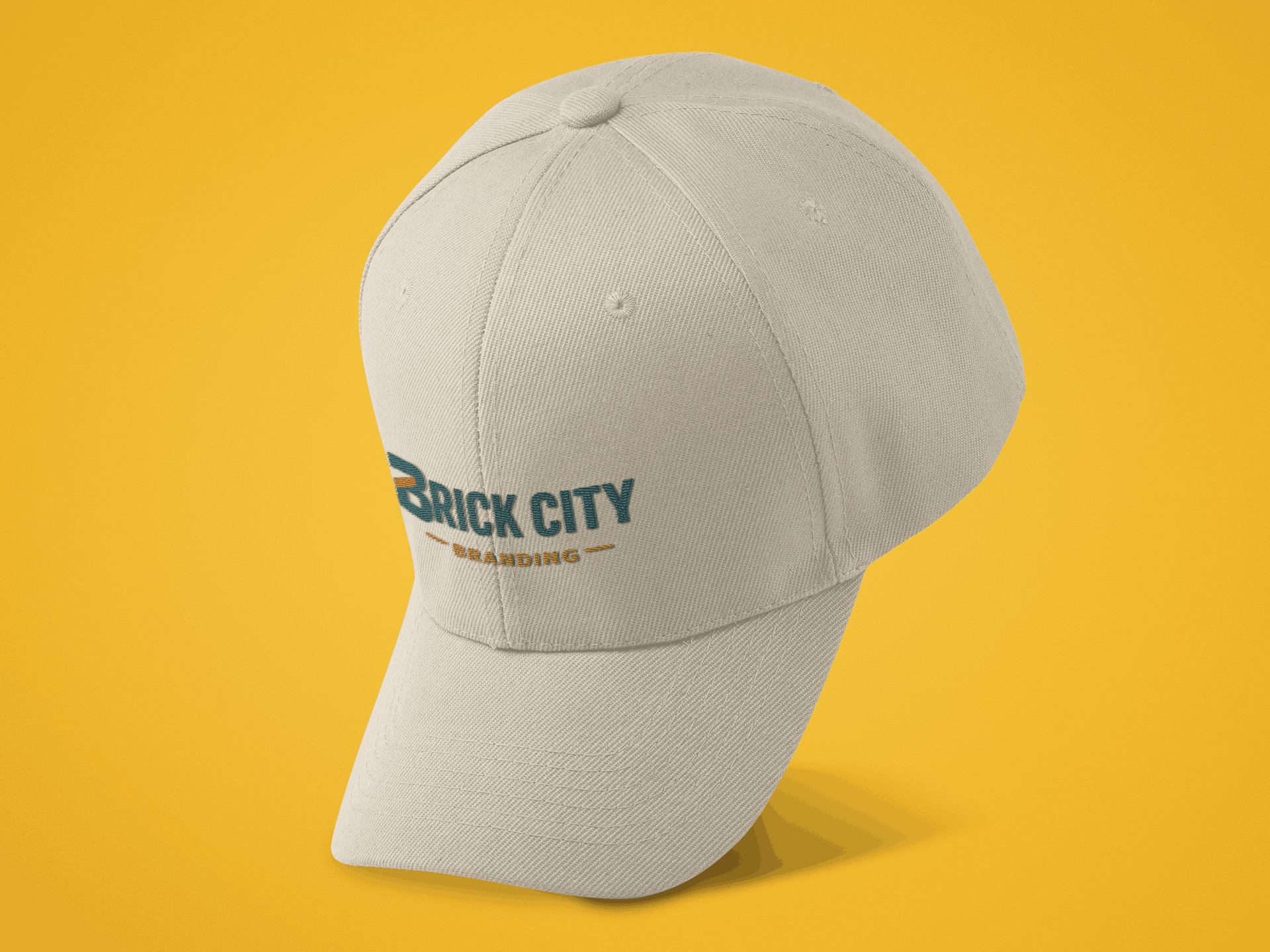 A cream-colored performance baseball cap with the Brick City Branding logo embroidered on the side panel, displayed at an angle against a vibrant yellow background.