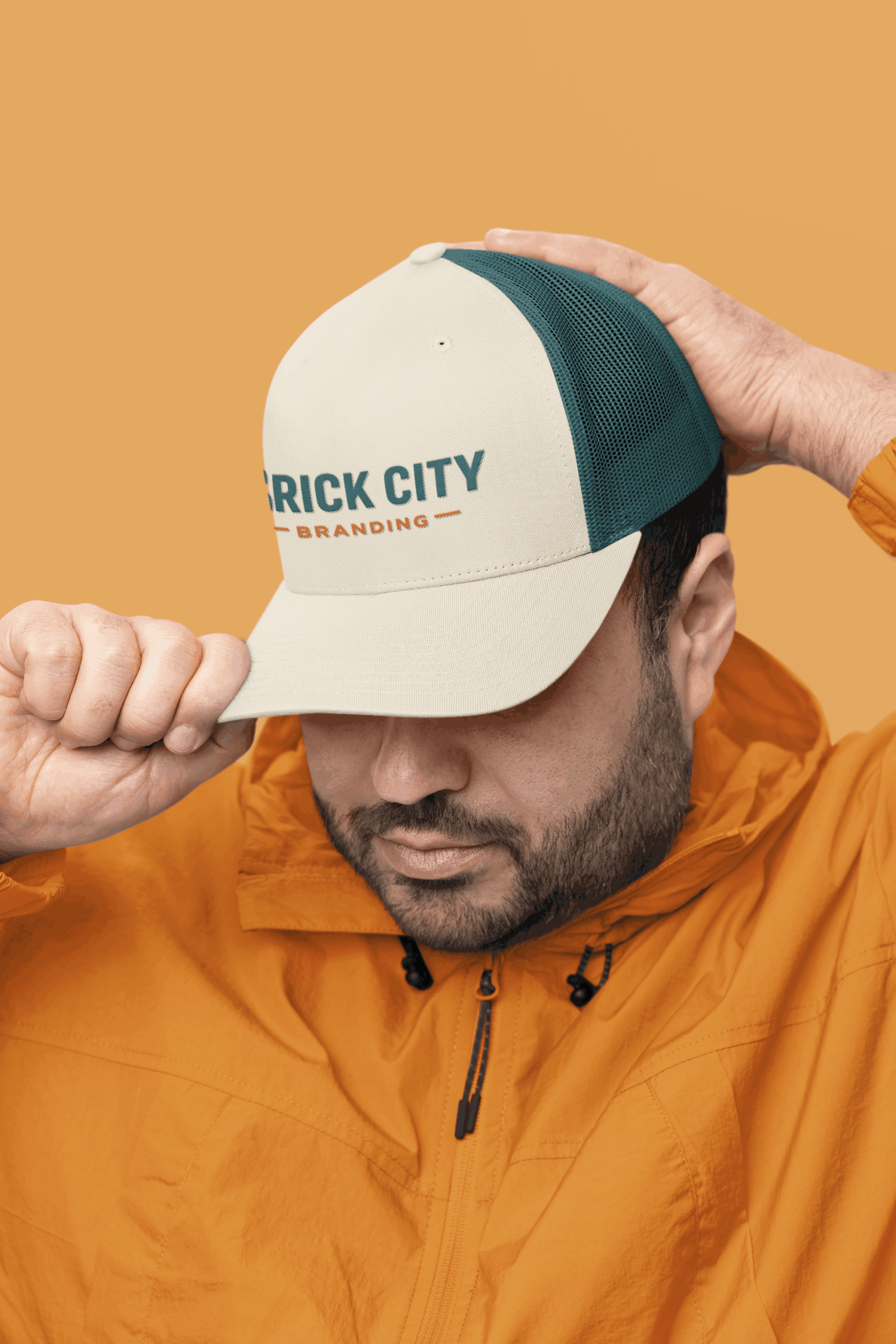 Man adjusting a cream and teal trucker hat with an embroidered logo