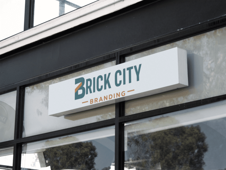 A horizontal white rectangular outdoor sign for "Brick City Branding" mounted on a modern black storefront, featuring a teal and orange "B" logo.