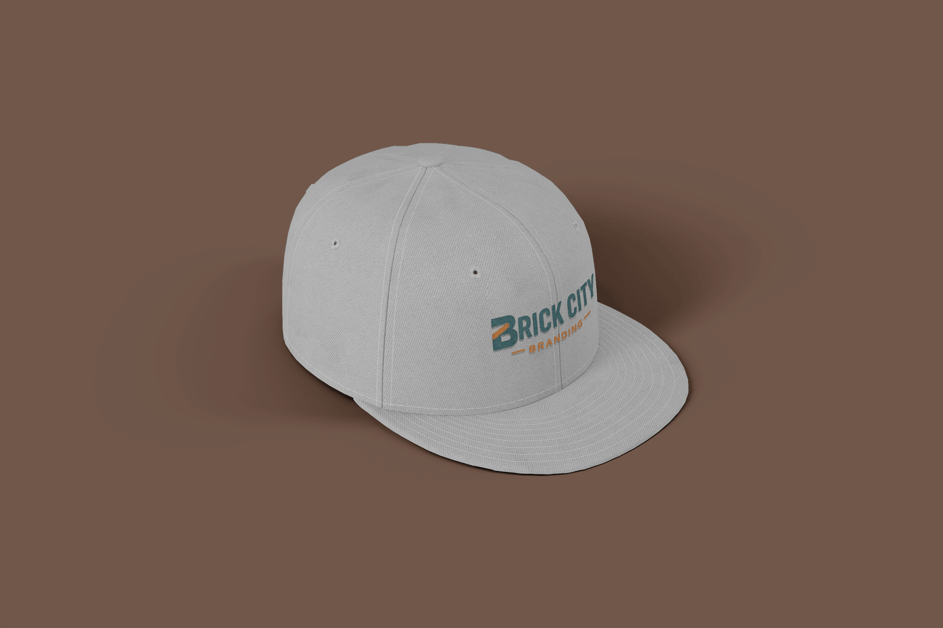 A tan-colored structured baseball cap with the "Brick City Branding" logo embroidered on the front, set against a warm yellow background.