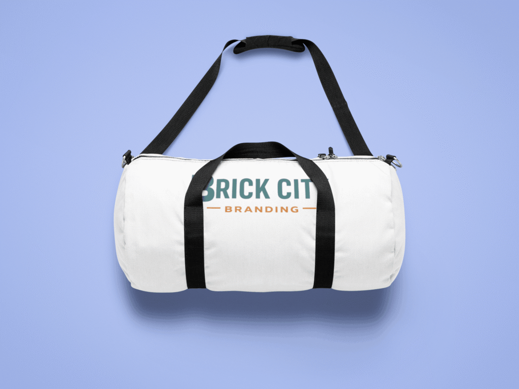 A white canvas cylindrical duffel bag with black straps featuring the Brick City Branding logo on the side, isolated on a lavender-blue background.
