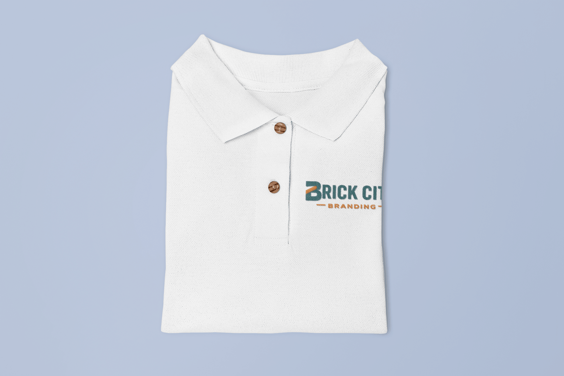 A folded white polo shirt with a high-quality multi-color embroidered "Brick City Branding" logo in teal and orange on the left chest.
