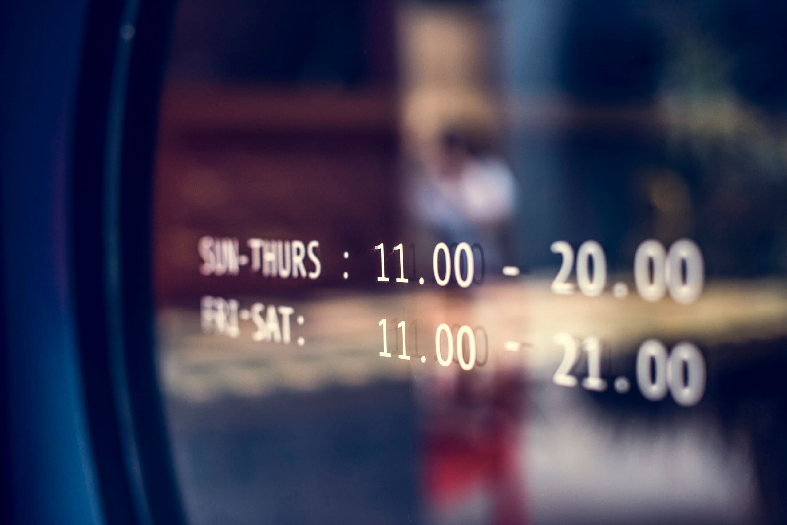 Close-up of white vinyl business hours printed on a glass door, showing operating times from 11:00 to 20:00 and 21:00.