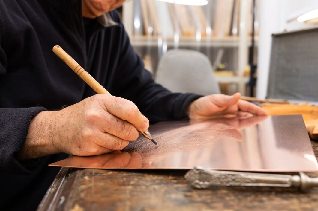 Artisan hand-engraving a custom logo onto a polished copper plate on a wooden workbench in Newark, NJ.