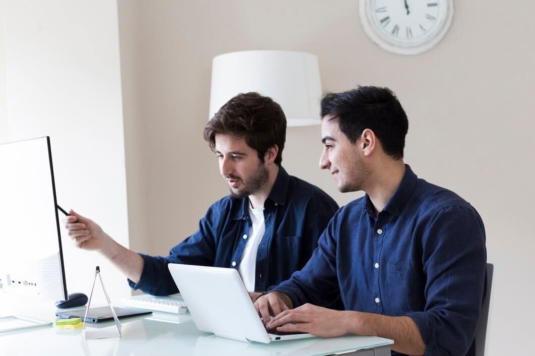 Two professionals collaborating at a modern desk with a computer monitor and laptop while discussing web development services in Austin, TX.