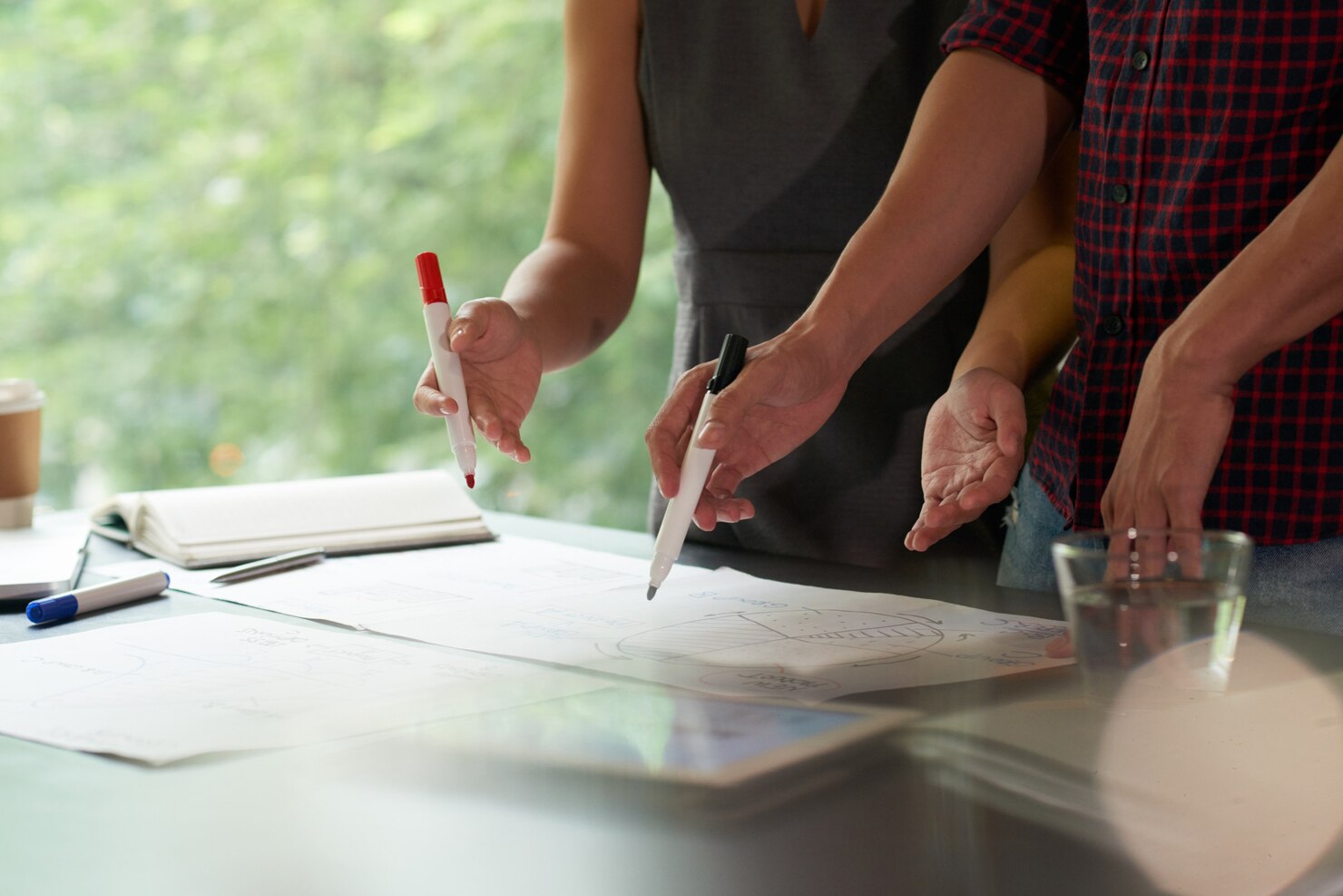 Close-up of two professionals using markers to point at printed data charts and a pie graph on a desk during a collaborative strategy meeting.