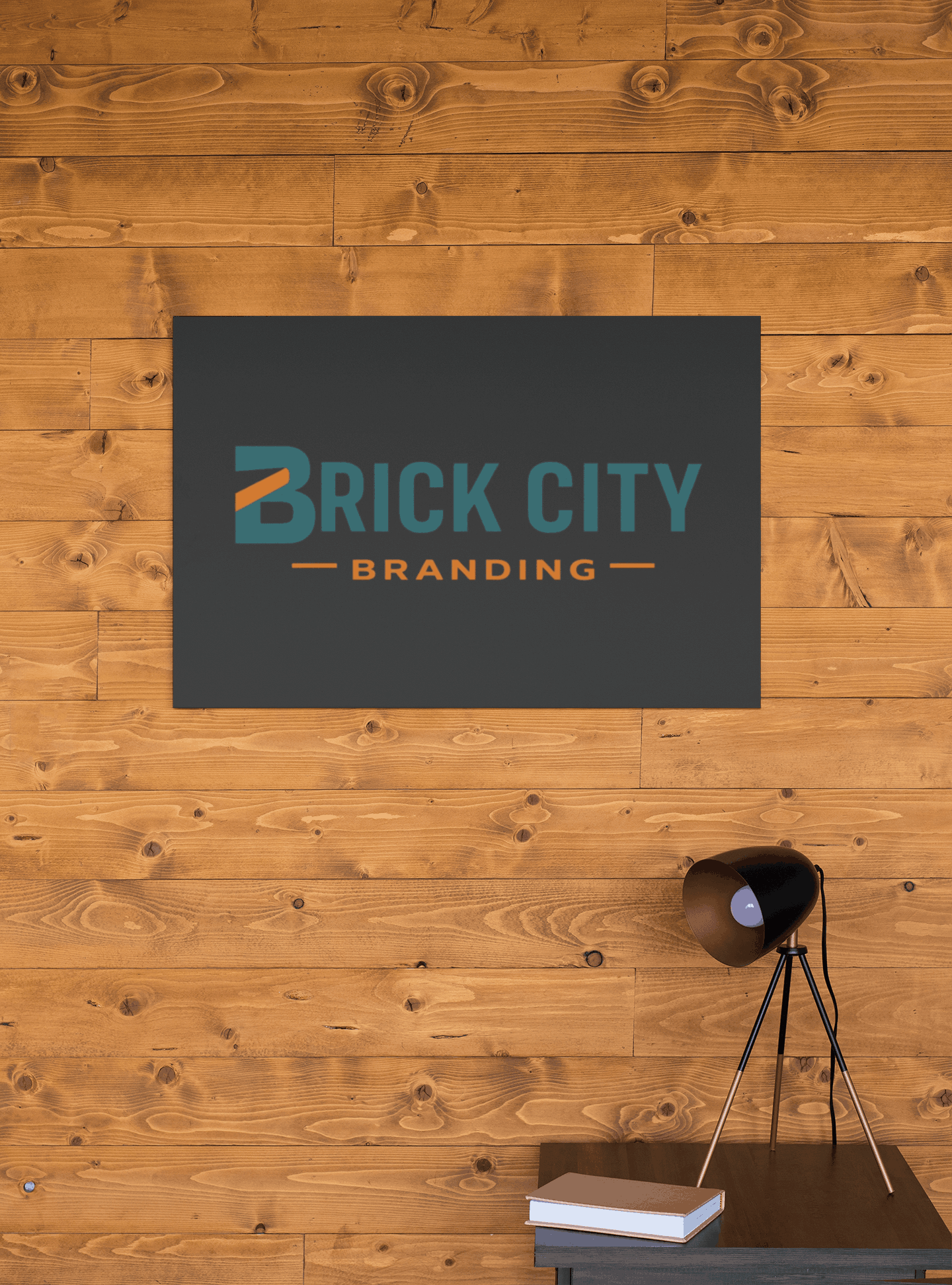 Matte charcoal grey office wall sign with teal and orange Brick City Branding logo from our blog page, mounted on a horizontal light wood plank accent wall.