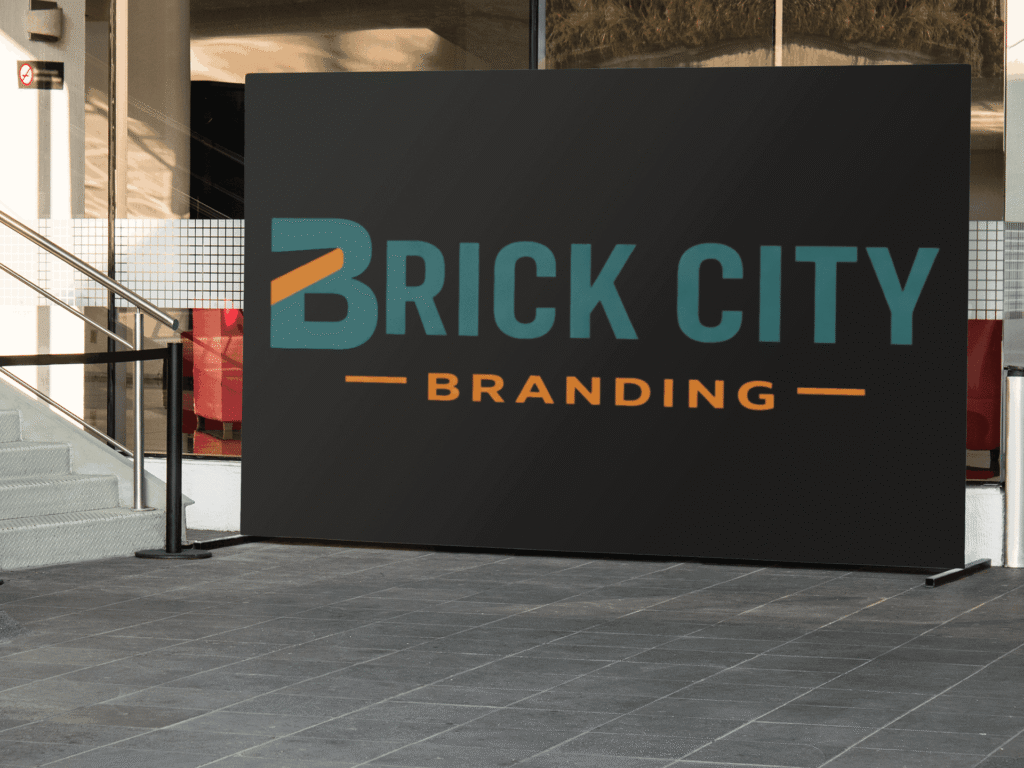 A large, matte black rectangular trade show backdrop featuring the Brick City Branding logo in teal and orange, positioned on a modern outdoor tiled plaza.