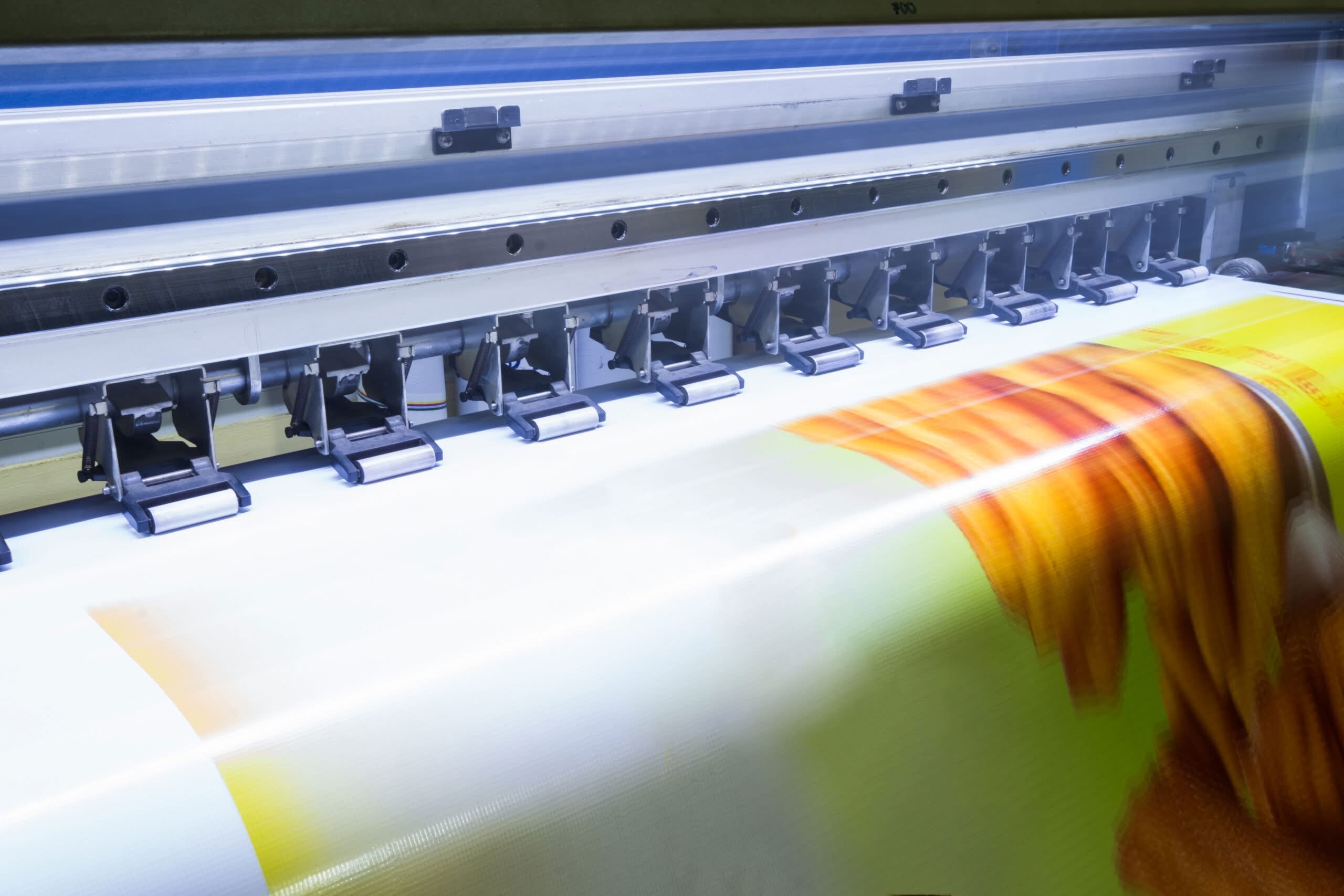 A large format industrial printer actively feeding and printing vibrant high-resolution graphics, illustrating commercial printing services in Dallas, TX.