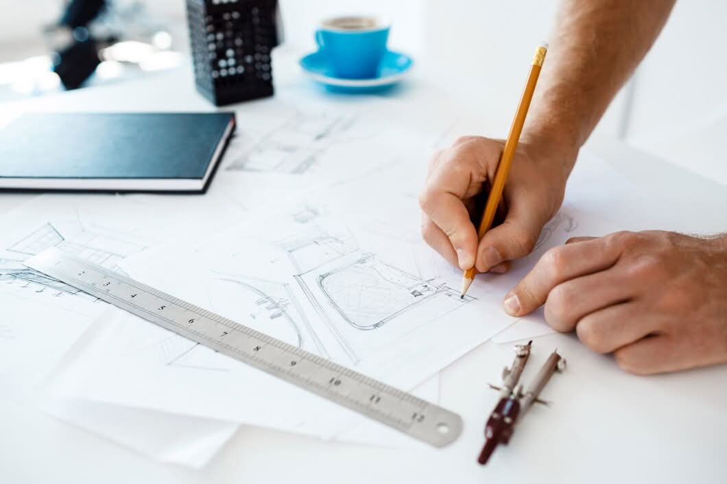 Designer sketching custom logo concepts with a pencil, ruler, and drafting compass on a desk in Newark, NJ.