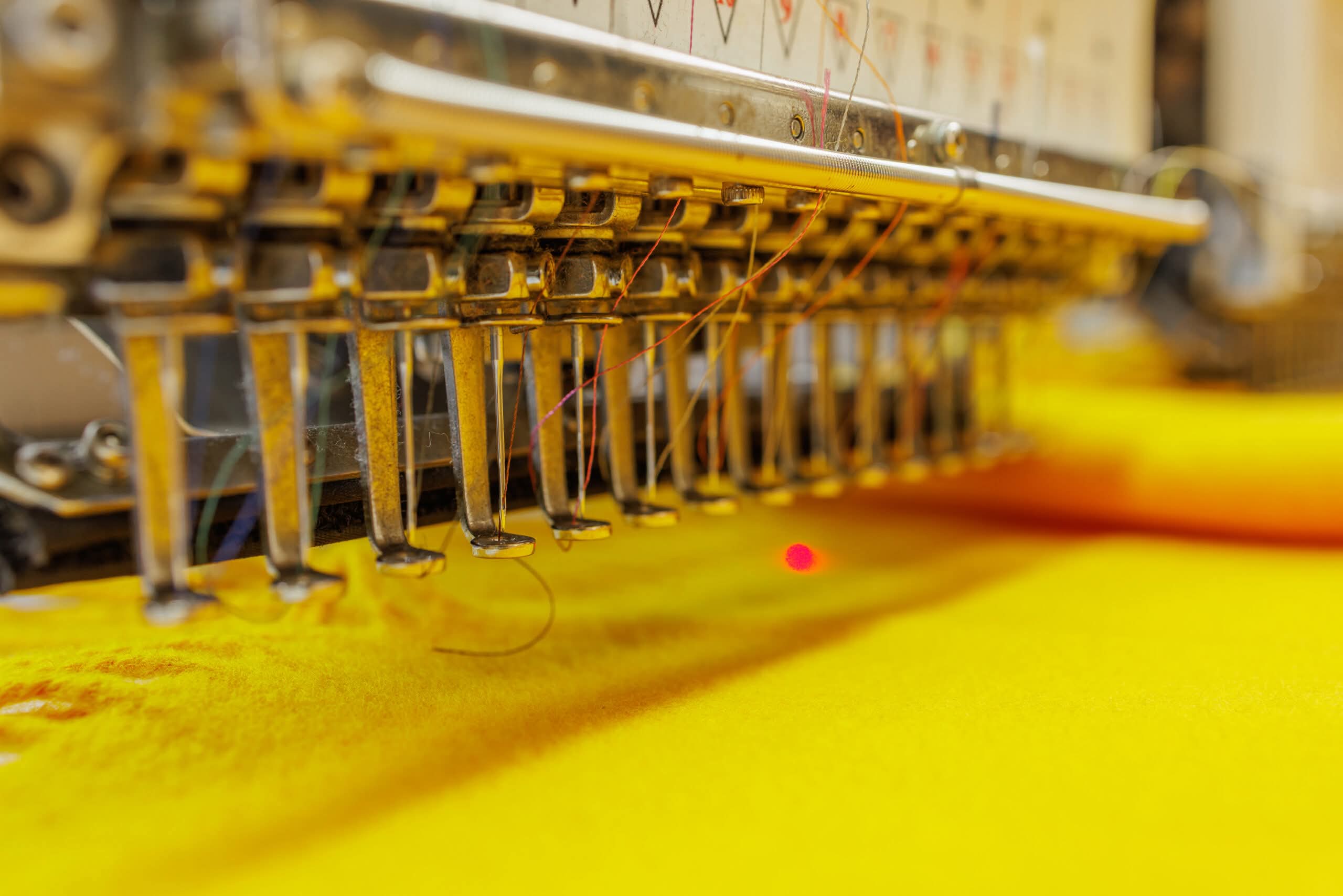 A close-up view of a multi-needle commercial embroidery machine stitching intricate designs on bright yellow fabric, illustrating commercial embroidery machine services in Nashville, TN.