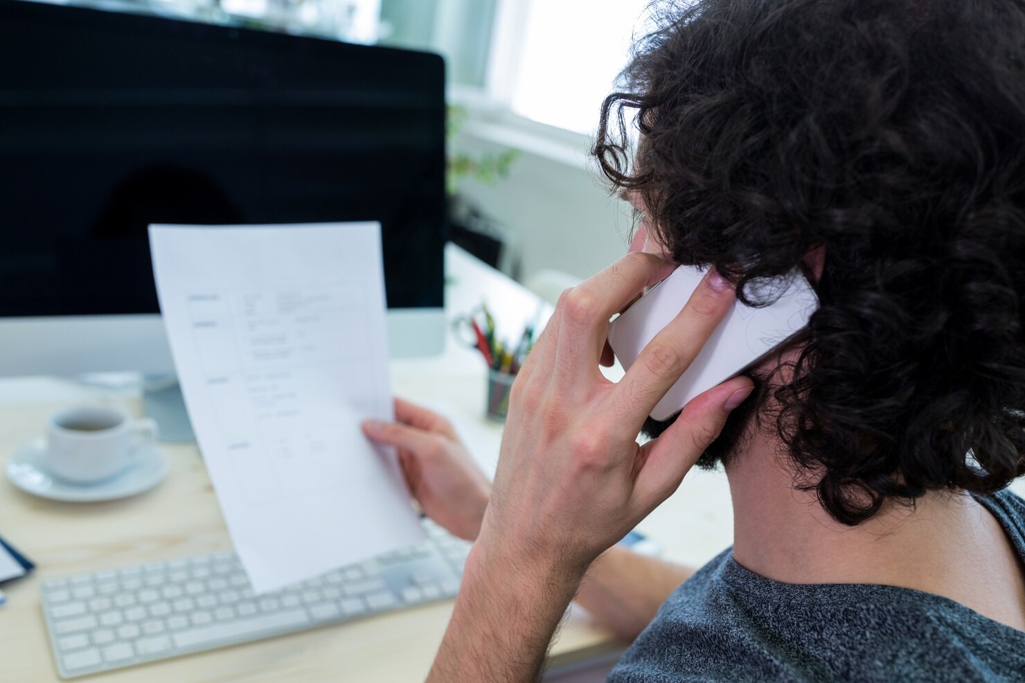 A creative consultant holding a document while talking on the phone at a office desk in Newark, NJ.