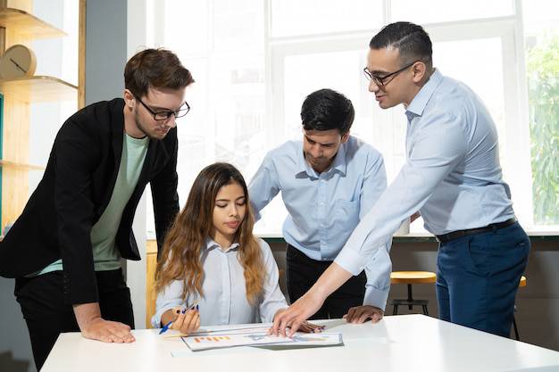 A diverse team of young professionals collaborating over printed marketing charts and brand strategy documents in a bright, modern office.