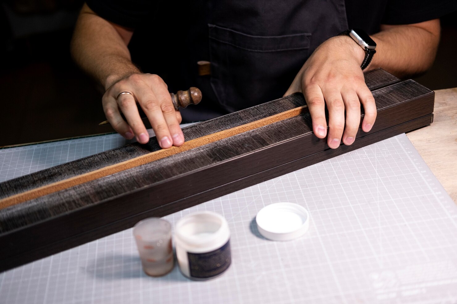 Artisan hand-burnishing a custom leather strap edge using a wooden slicker on a workbench in Newark, NJ.