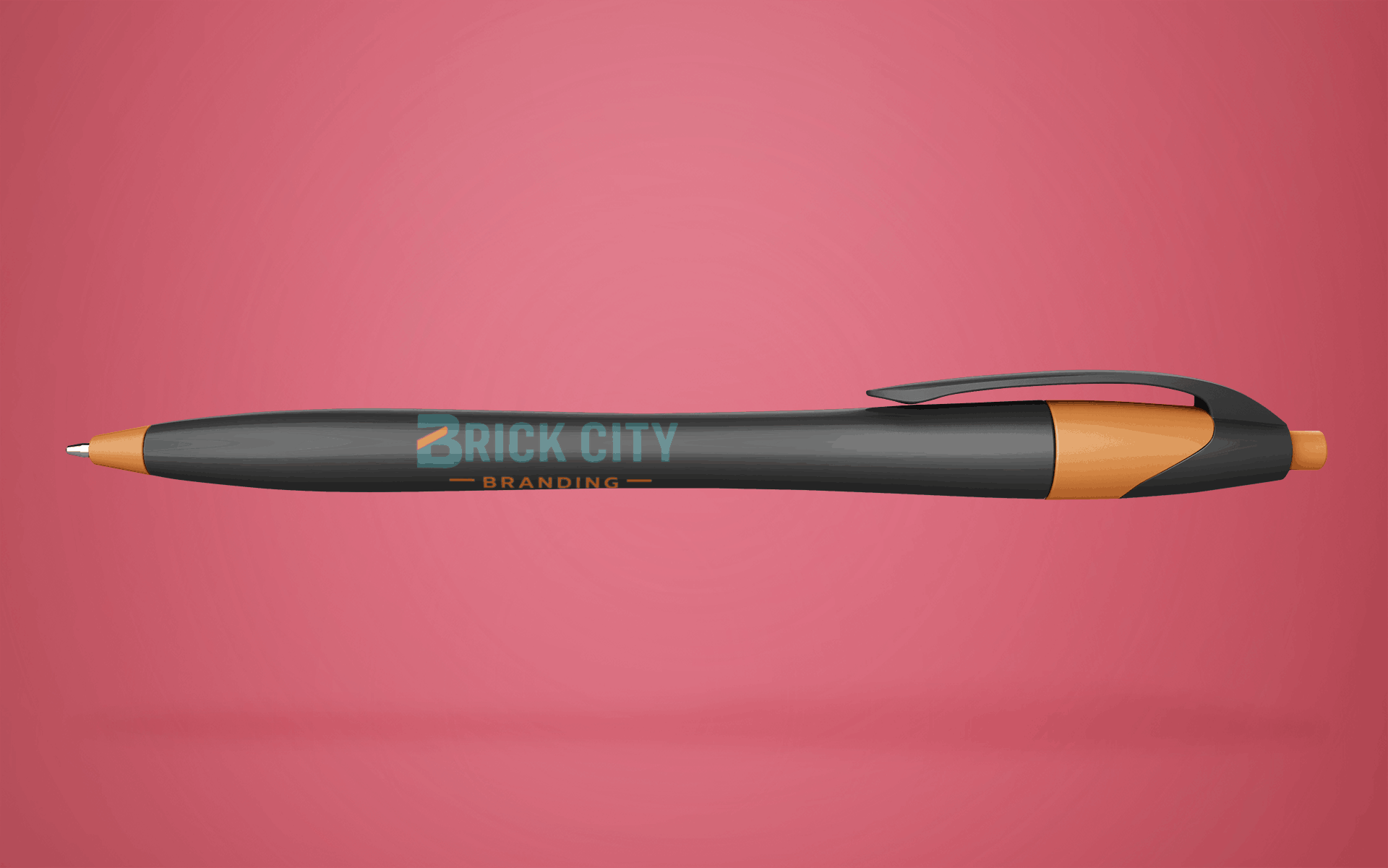 A soft-touch rubberized black ballpoint pen with vibrant orange accents and the Brick City Branding logo on the barrel.