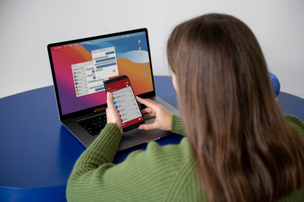 Woman holding a smartphone while working on a laptop displaying a messaging app in Newark, NJ.