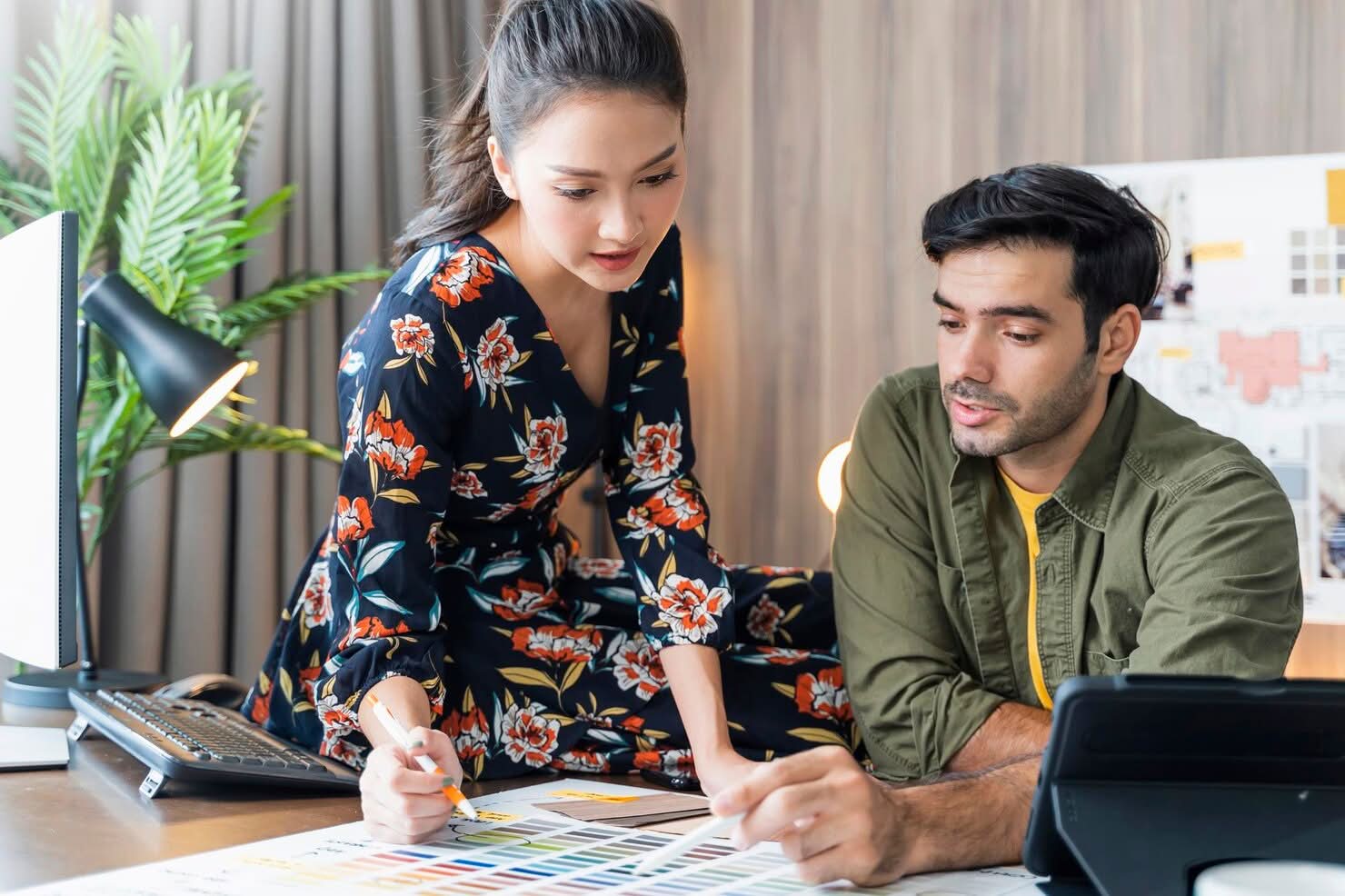 A male and female designer analyzing color palettes and mood boards together at a workspace, representing an interior design firm in Seattle, WA.