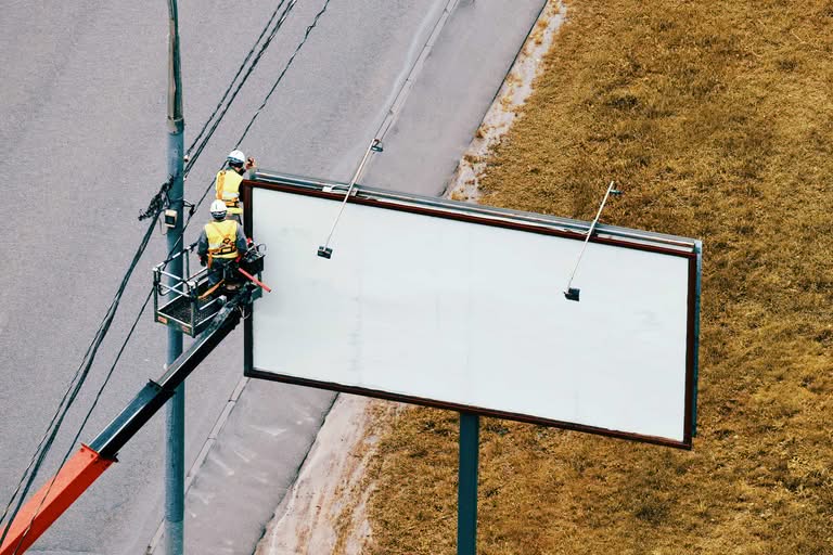 Workers in safety gear installing an outdoor advertisement on a roadside billboard in Ocala sign companies.